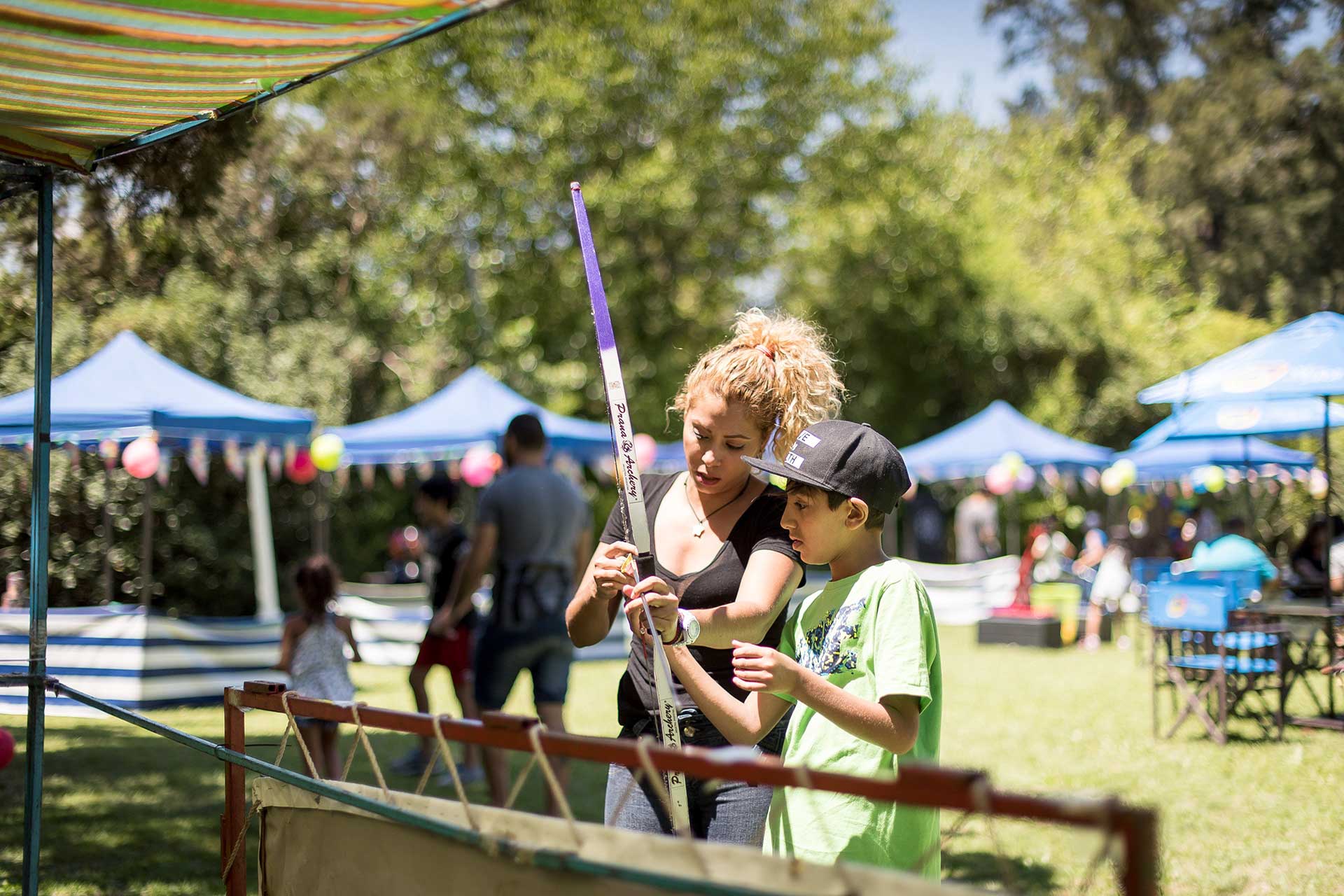 Fotografía de una madre explicándole a su hijo como utilizar un arco y flecha para uno de los juegos presentes en el evento, matutino, organizado por la empresa 'Danone Argentina'