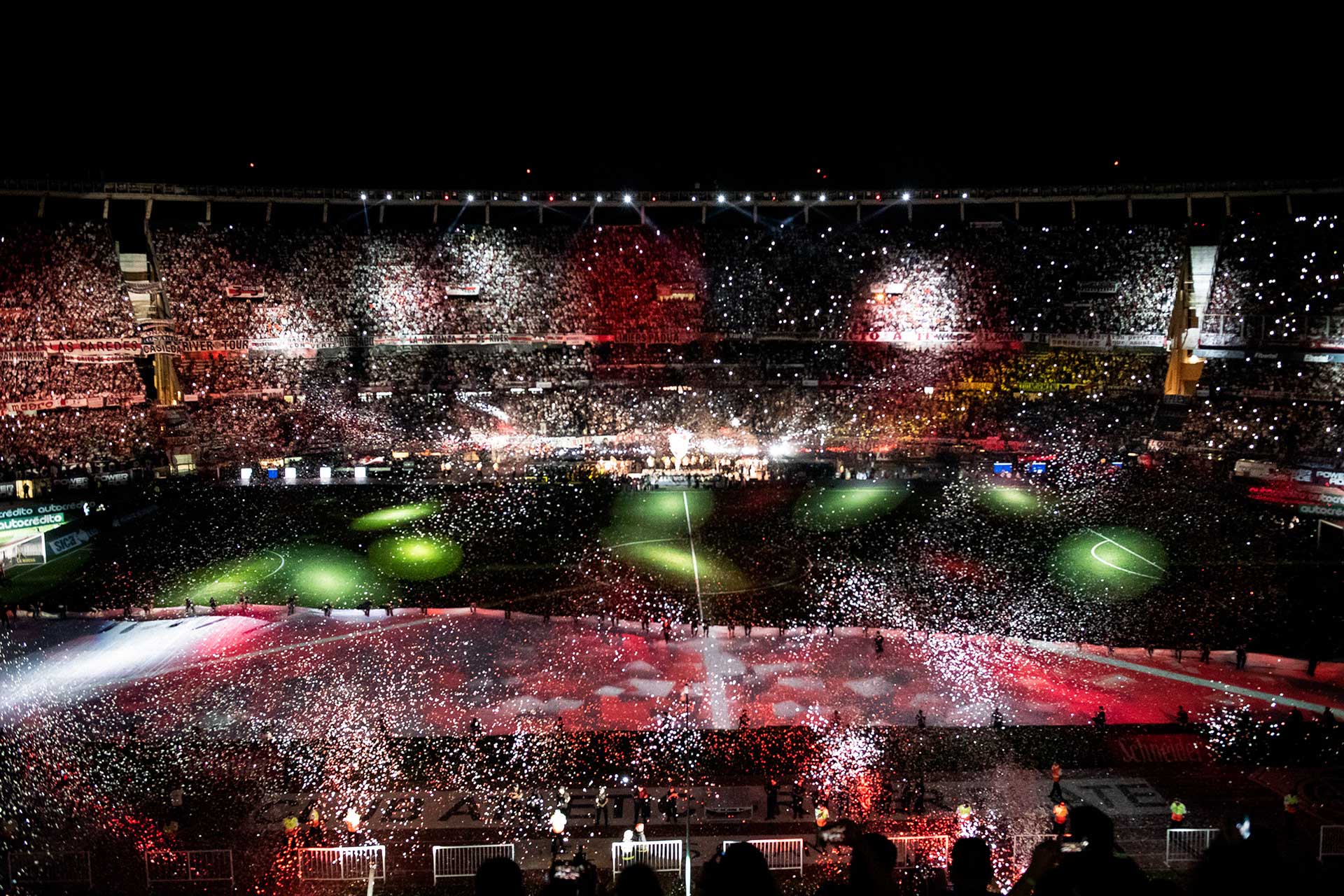 Fotografía del despliegue de la manta, donde se proyectan imágenes, sobre el terreno de juego. De Fondo las tribunas llenas acompañadas de una lluvia de papelitos y juegos de luces. Cobertura del evento '09-12 eterno' organizado por el Club Atlético River Plate