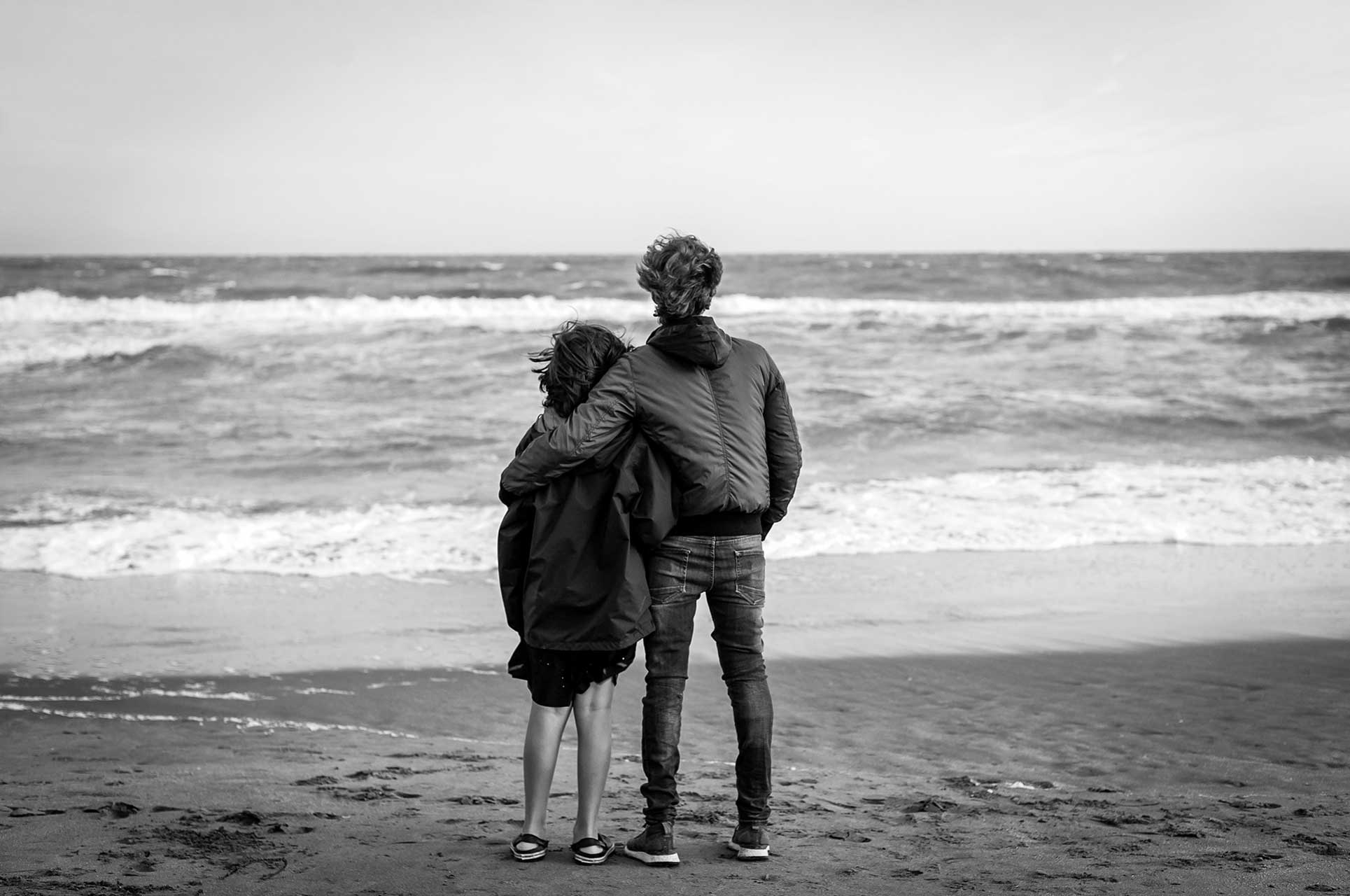 Fotografía, en blanco y negro, de padre e hijo mirando al horizonte en la orilla de una playa