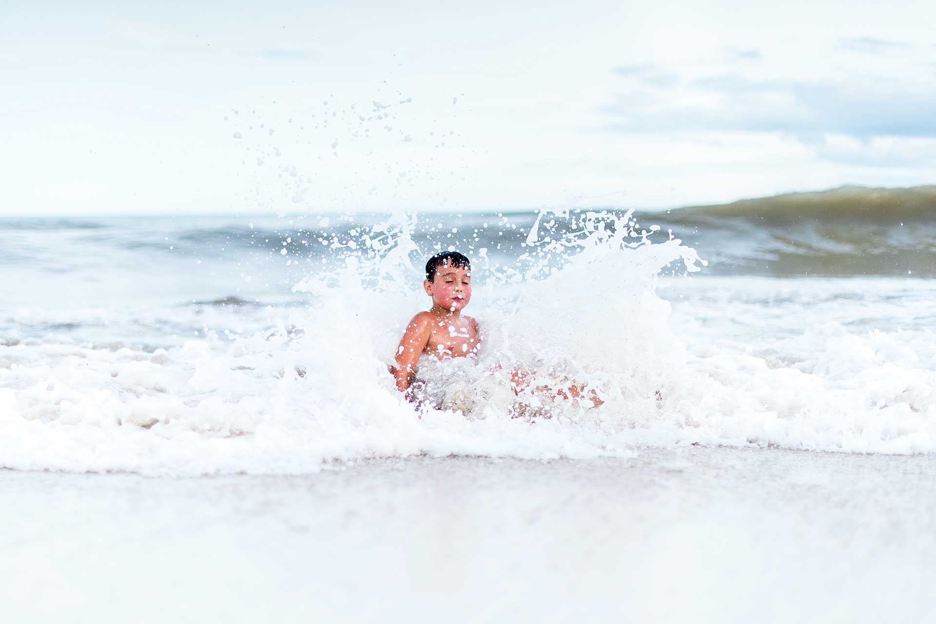 Fotografía, en primer plano, de un niño embestido por una ola en la orilla de una playa