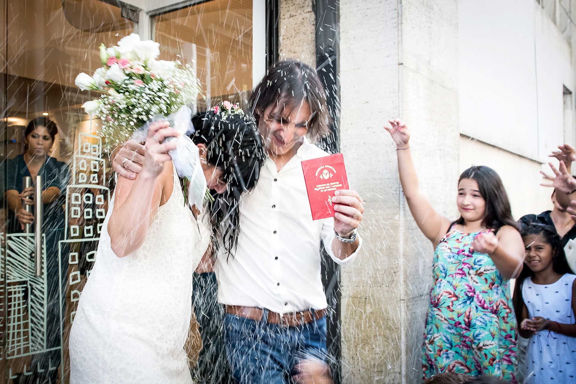 Fotografía del momento en que los novios salen del Registro Civil con la libreta de matrimonio en alto. Familiares y amigos les arrojan el tradicional arroz. Casamiento de Noe y Ale