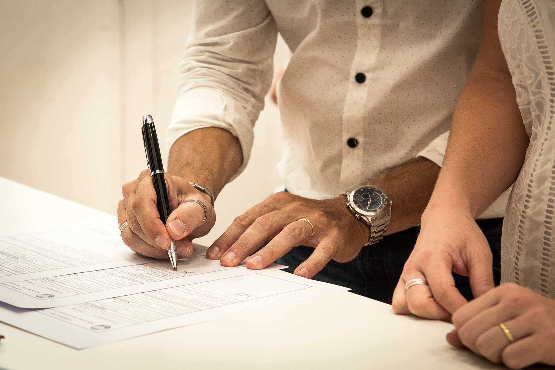 Fotografía, en primer plano, de las manos del novio firmando el acta de matrimonio, a su lado las manos de su futura mujer. Casamiento de Noe y Ale