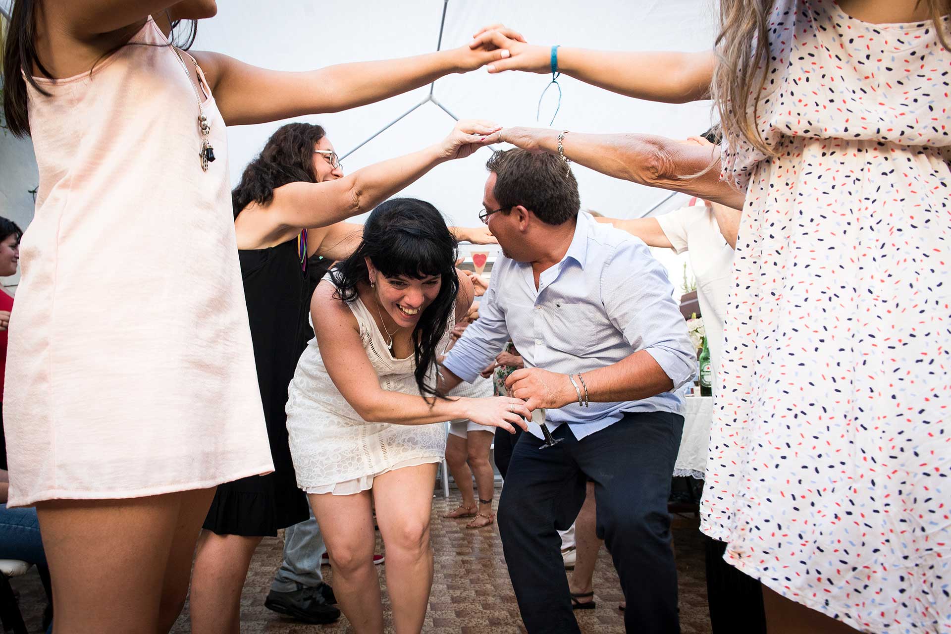 Fotografía de la novia y un amigo atravesando, felices, un puente humano durante la fiesta de casamiento. Casamiento de Noe y Ale