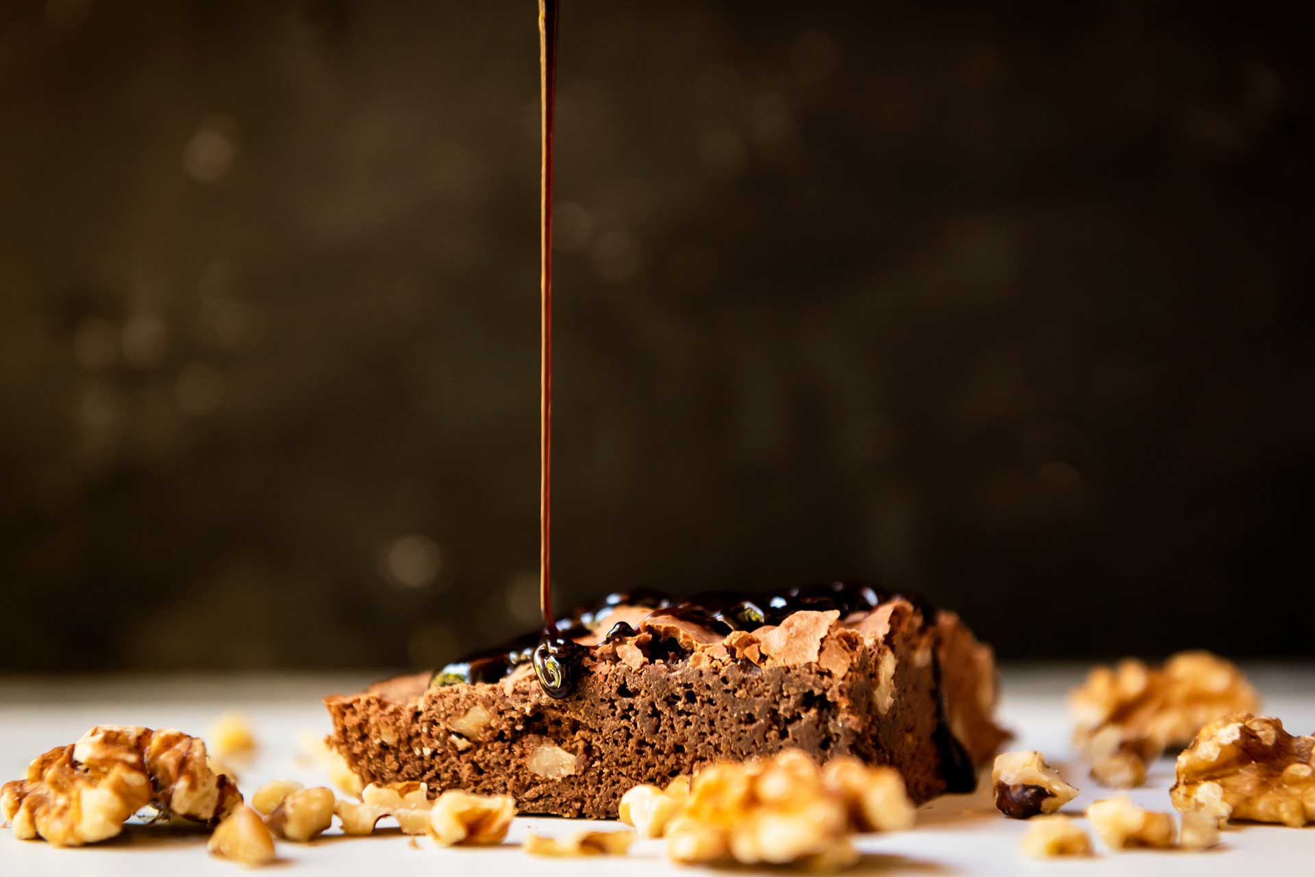 Fotografía de una porción de torta a la que se le está volcando una salsa de chocolate. Campaña para el emprendimiento 'Deli Luli - Delicatessen'