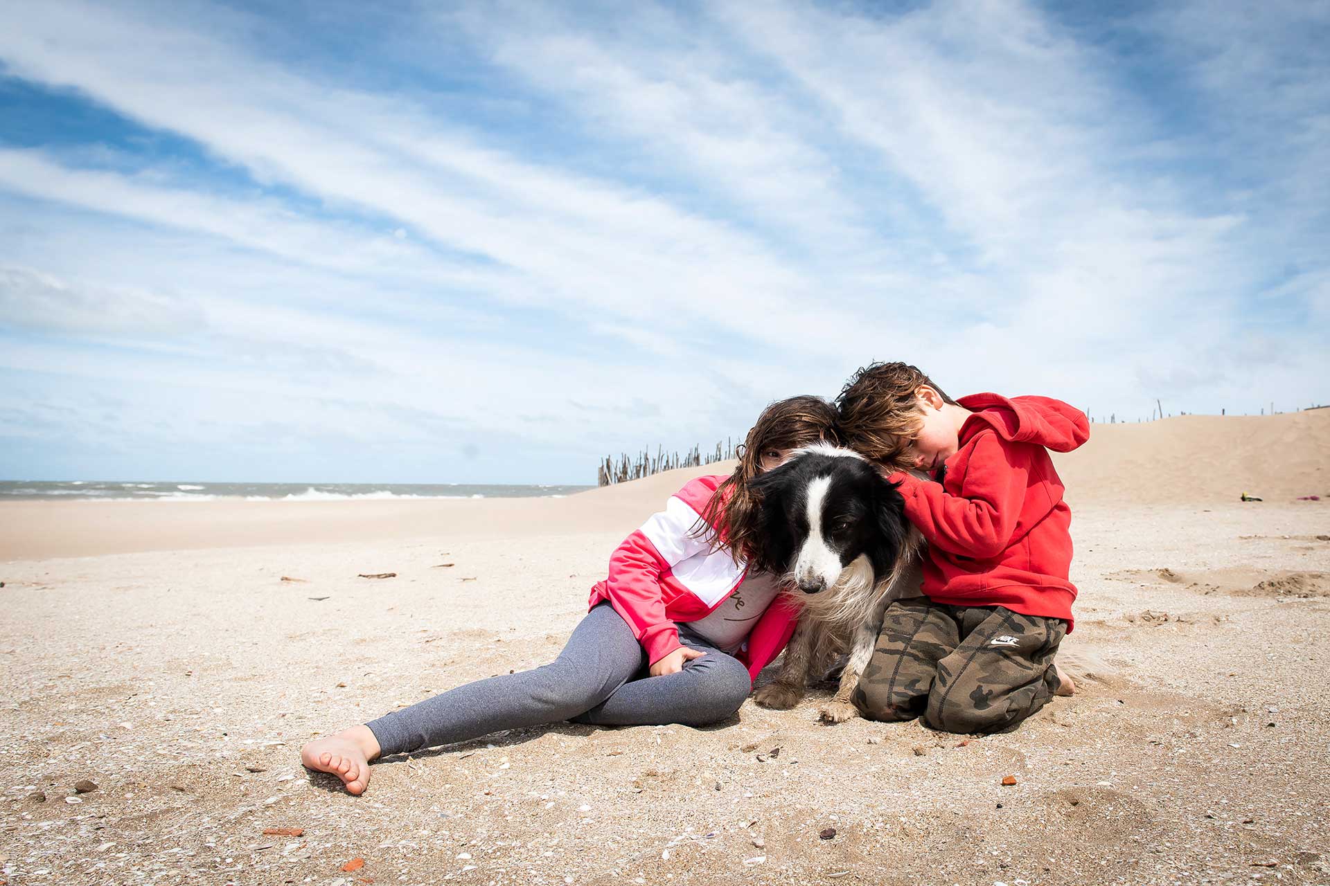 Amor perruno. Fotografía de dos primos recostados en la playa junto a un perro