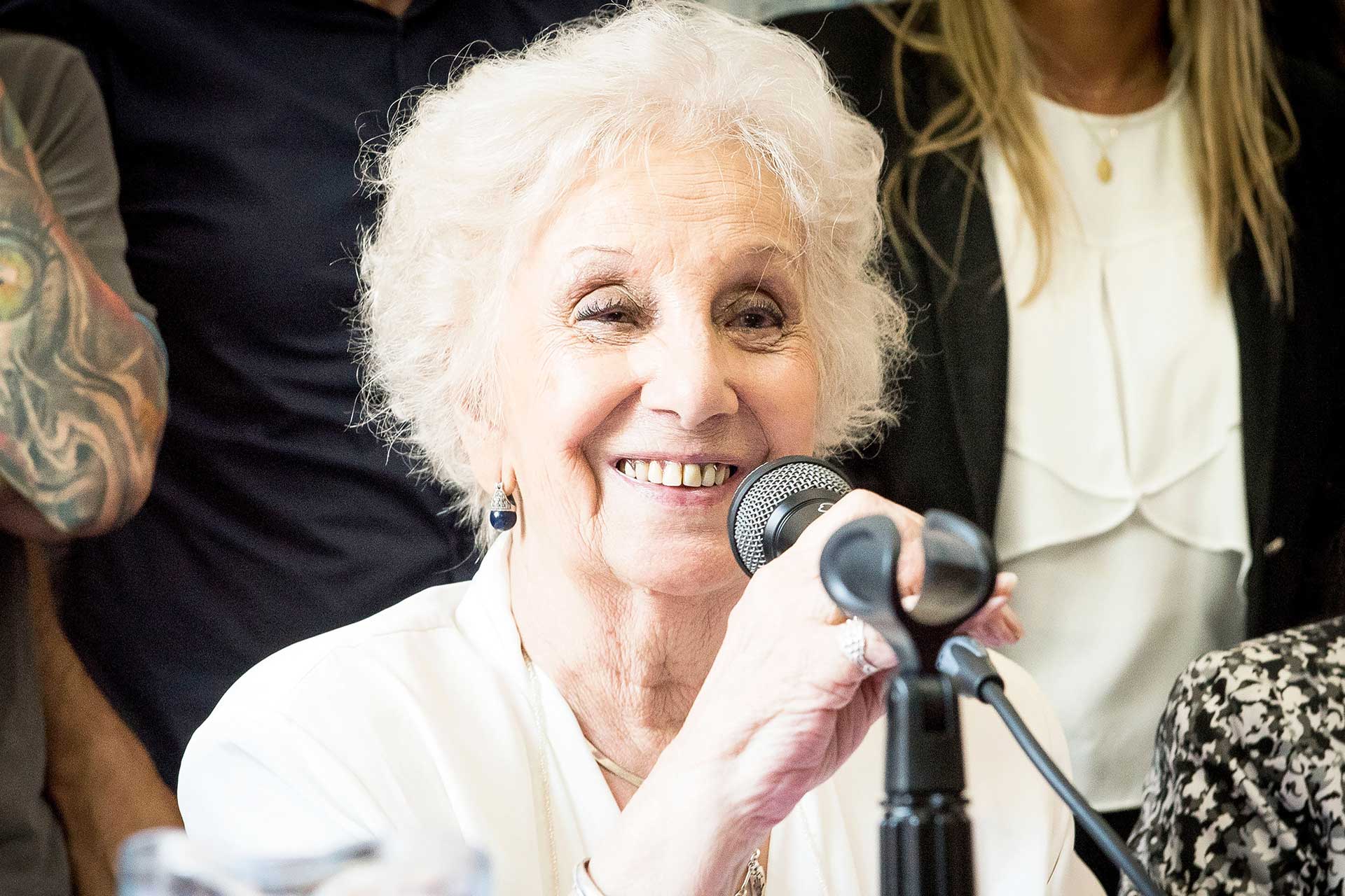 Retrato fotográfico de Estela de Carlotto, Presidenta de Abuelas de Plaza de Mayo, sosteniendo un micrófono durante un acto de restitución de un nieto apropiado por la última dictadura cívico-militar en la República Argentina