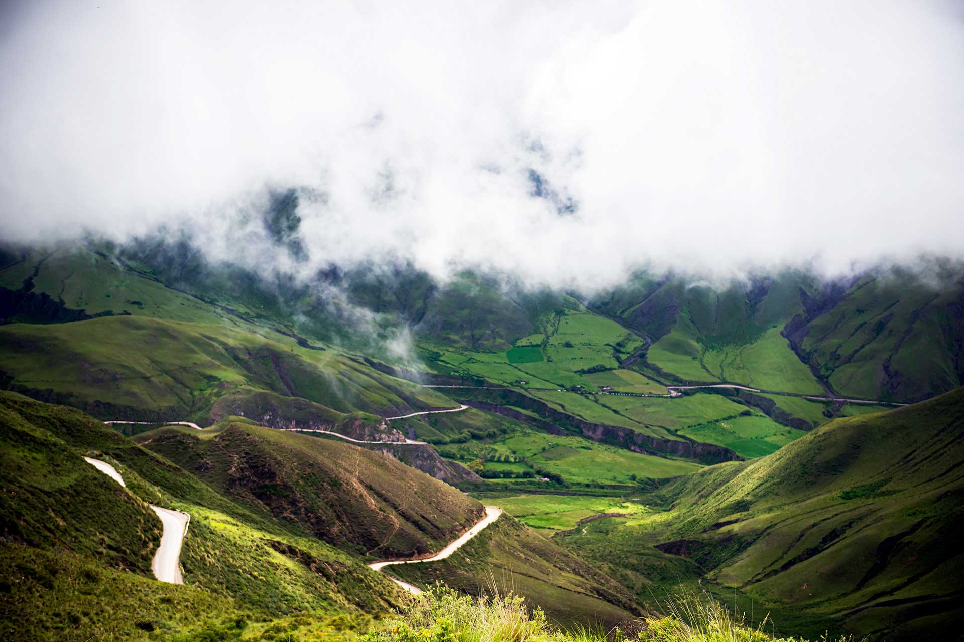 Fotografía de la Cuesta del Obispo, Salta, Argentina. A plena luz del día con sus campos verdes iluminados y un colchón de nubes sobre la cima