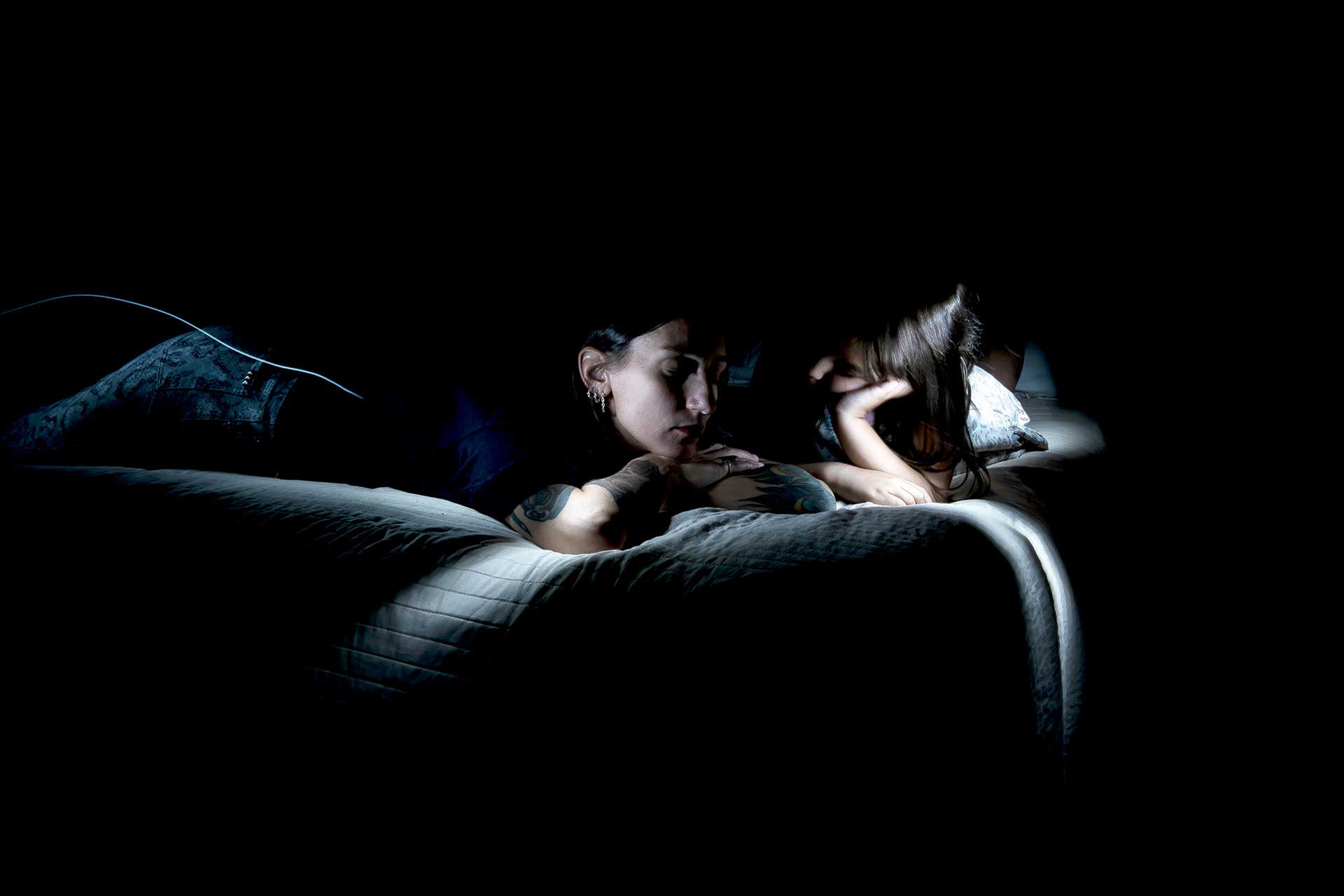 Fotografía de una niña y una mujer conversando en la oscuridad iluminada por un as de luz