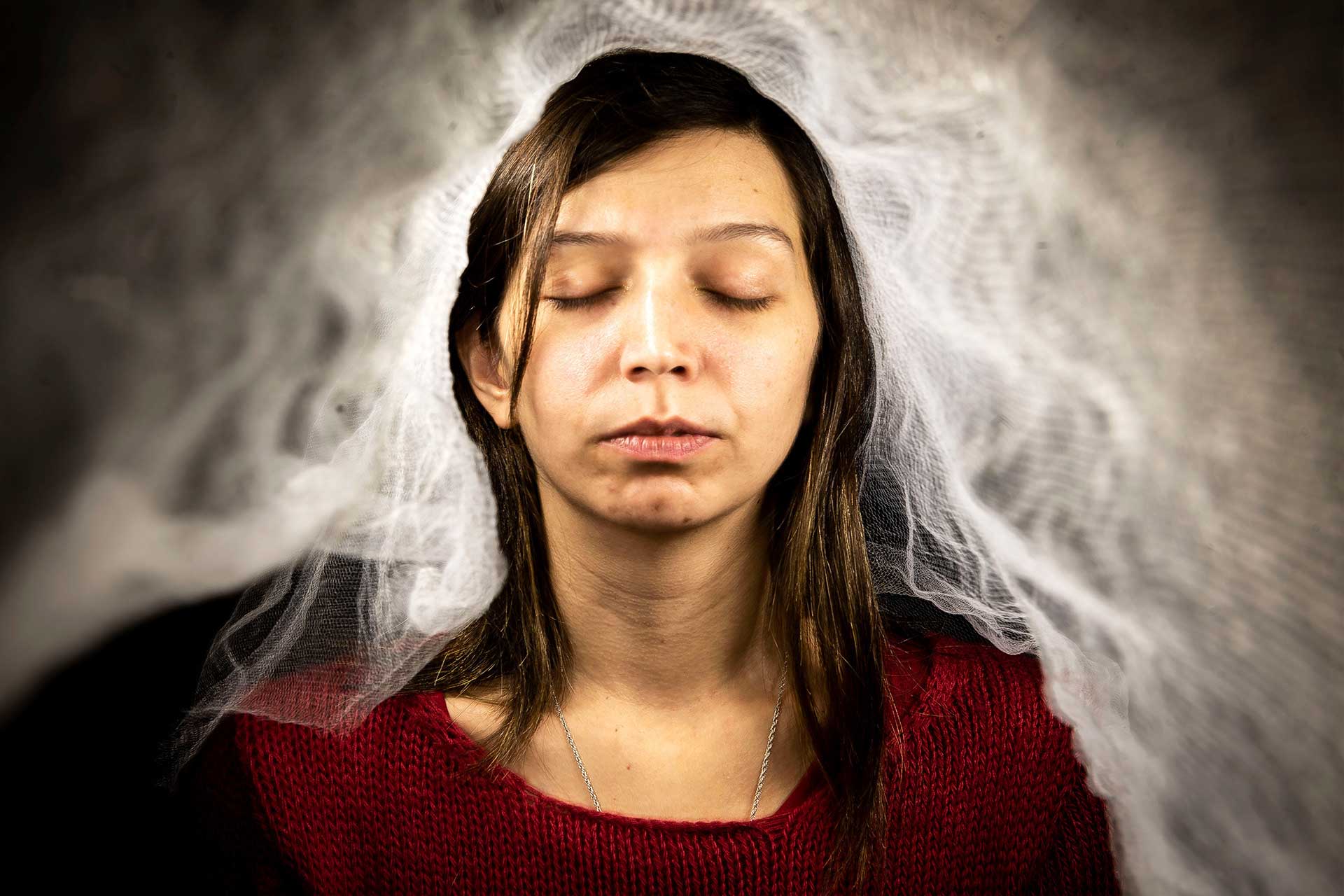 Retrato fotográfico de una mujer iluminada por un velo blanco en plena oscuridad